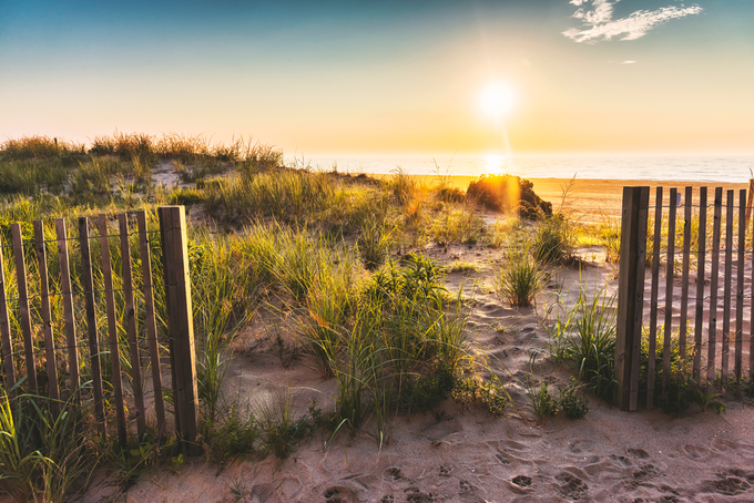 A wooden fence leading to a beach at sunset.