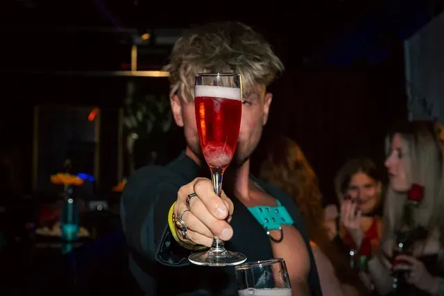 Un hombre sostiene una copa de vino tinto frente a su cara.