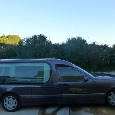 Un coche fúnebre de color violeta está estacionado al costado de la carretera.