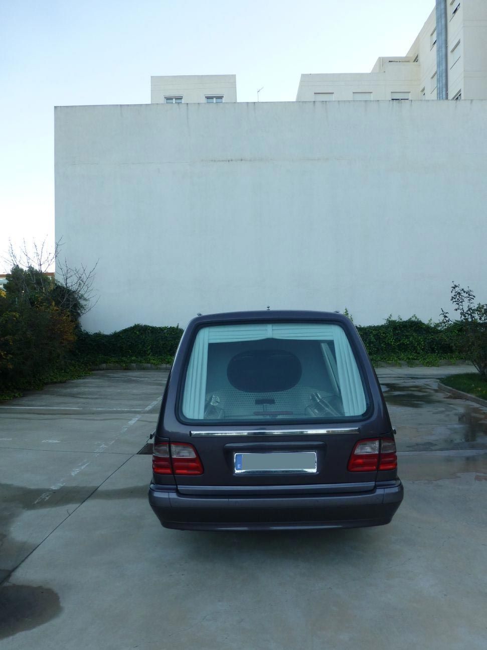 Un coche negro está aparcado en un estacionamiento con un edificio blanco al fondo.