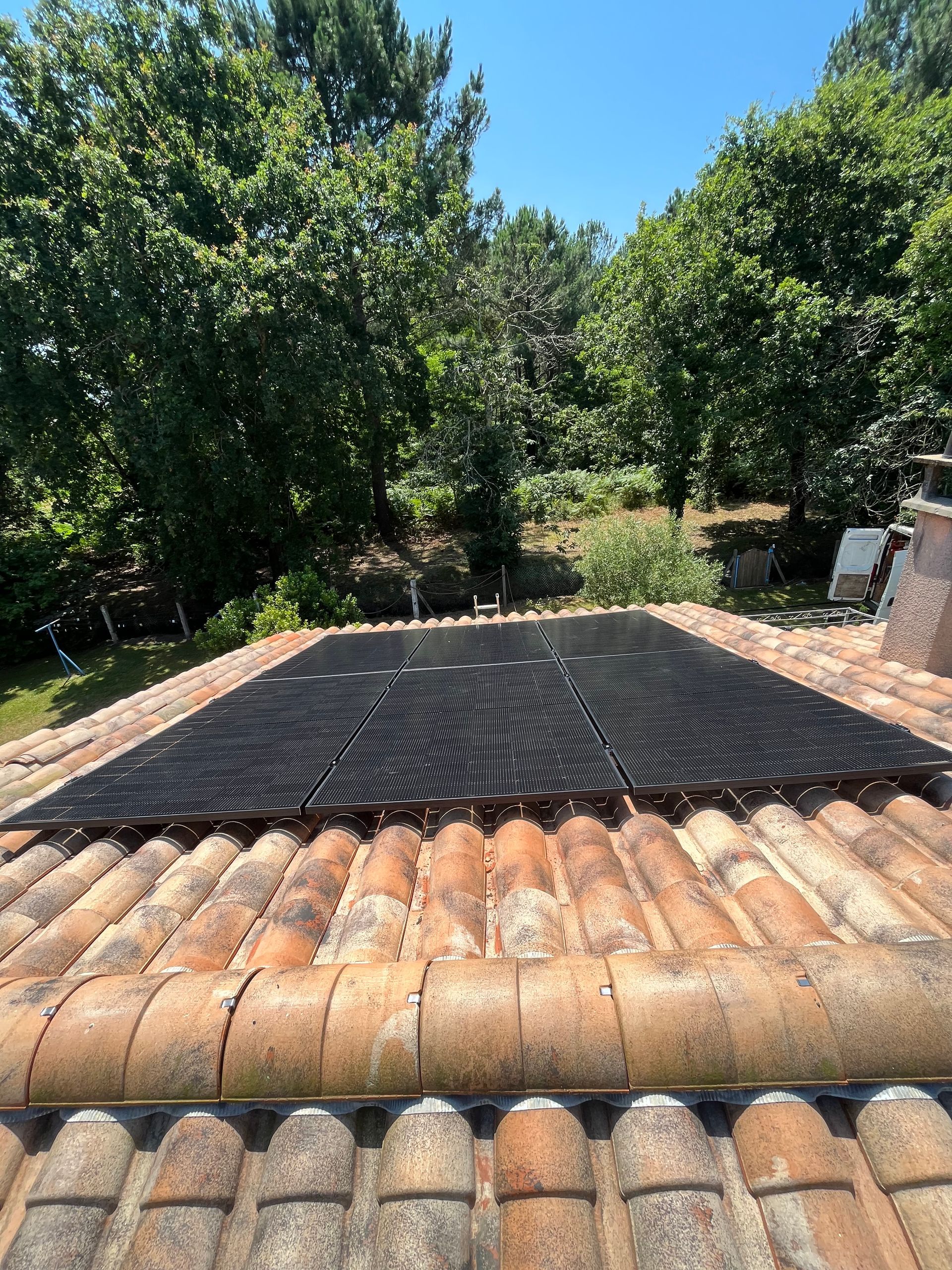 Panneaux photovoltaïques sur un toit de tuiles en terre cuite, avec des arbres et un ciel bleu en arrière-plan