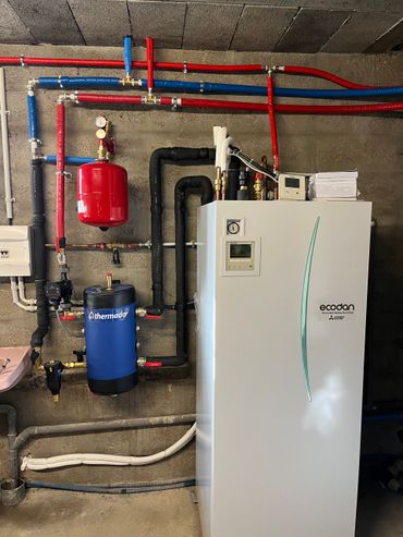 Chaufferie avec groupe de chauffage blanc, tuyaux rouges et bleus et réservoirs d'eau adossés à un mur en béton