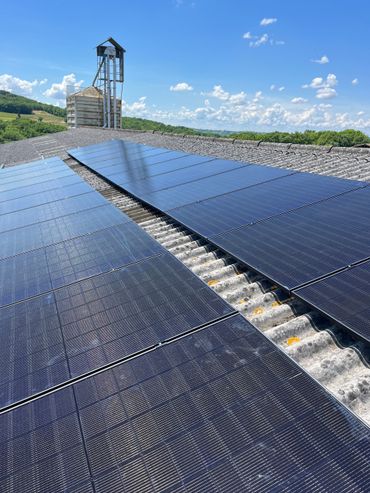 Des panneaux solaires dans un champ sous un ciel bleu, avec un pylône électrique en arrière-plan.