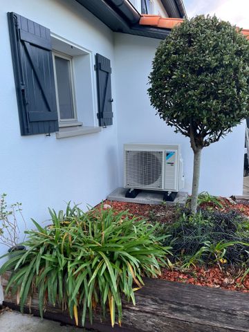 Maison à l'extérieur en stuc blanc avec volets bleus, climatiseur de fenêtre et jardin paysager à l'avant avec un arbre taillé.