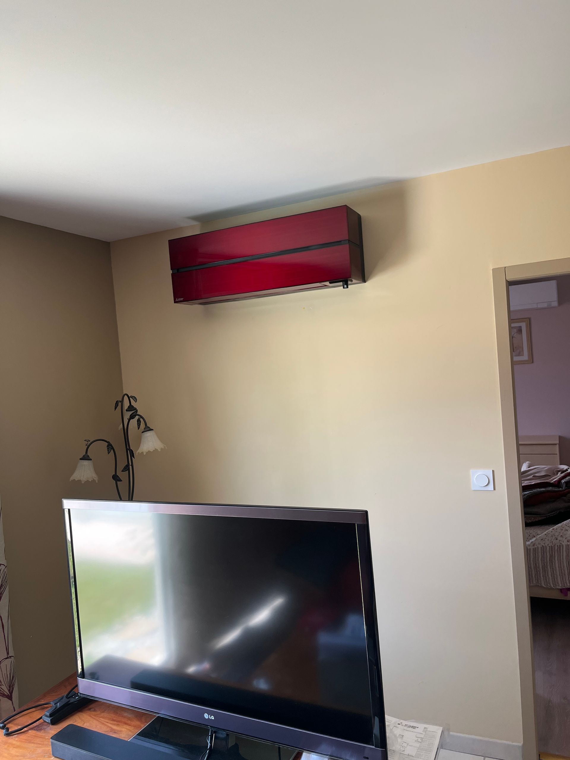Salon avec climatiseur rouge mural au-dessus d'une télévision et d'un lampadaire.