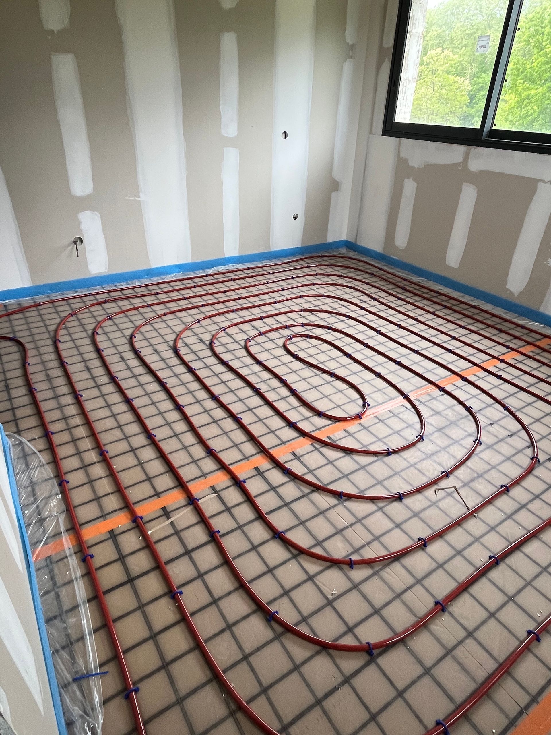 Petite pièce avec des cloisons sèches non finies et un serpentin de chauffage au sol rouge.