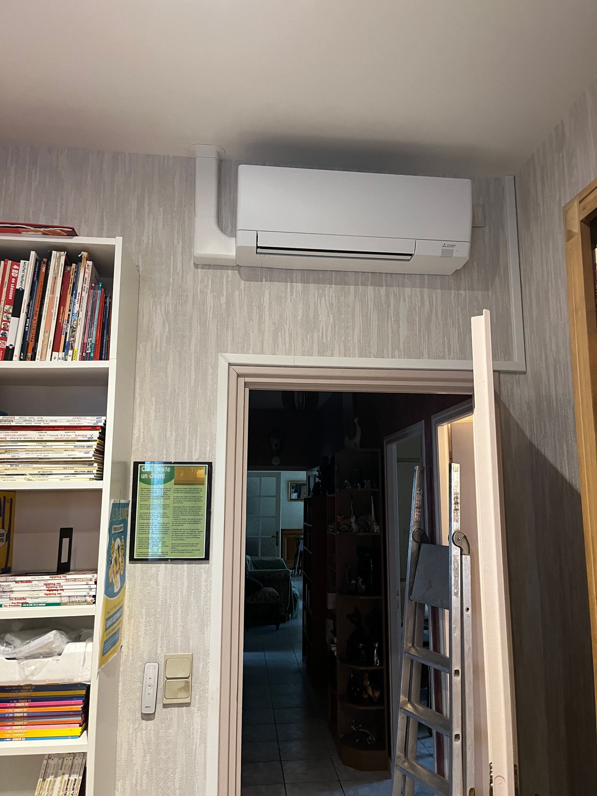 Climatiseur mural blanc au-dessus d'une porte dans une pièce avec étagères et échelle suspendue