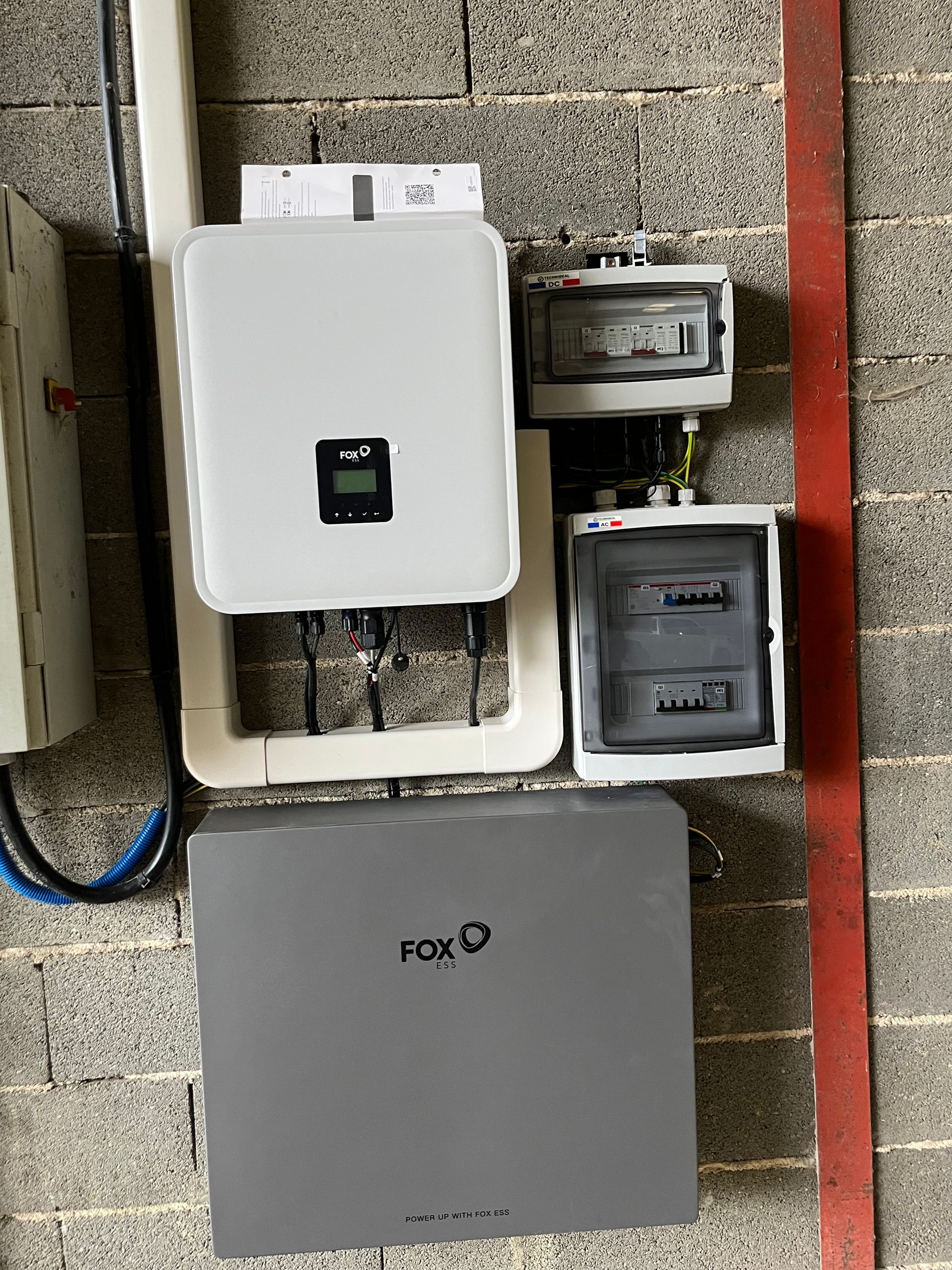 Des boîtiers électriques fixés sur un mur de pierre, à côté d'un trottoir rouge et d'un boîtier Fox gris.