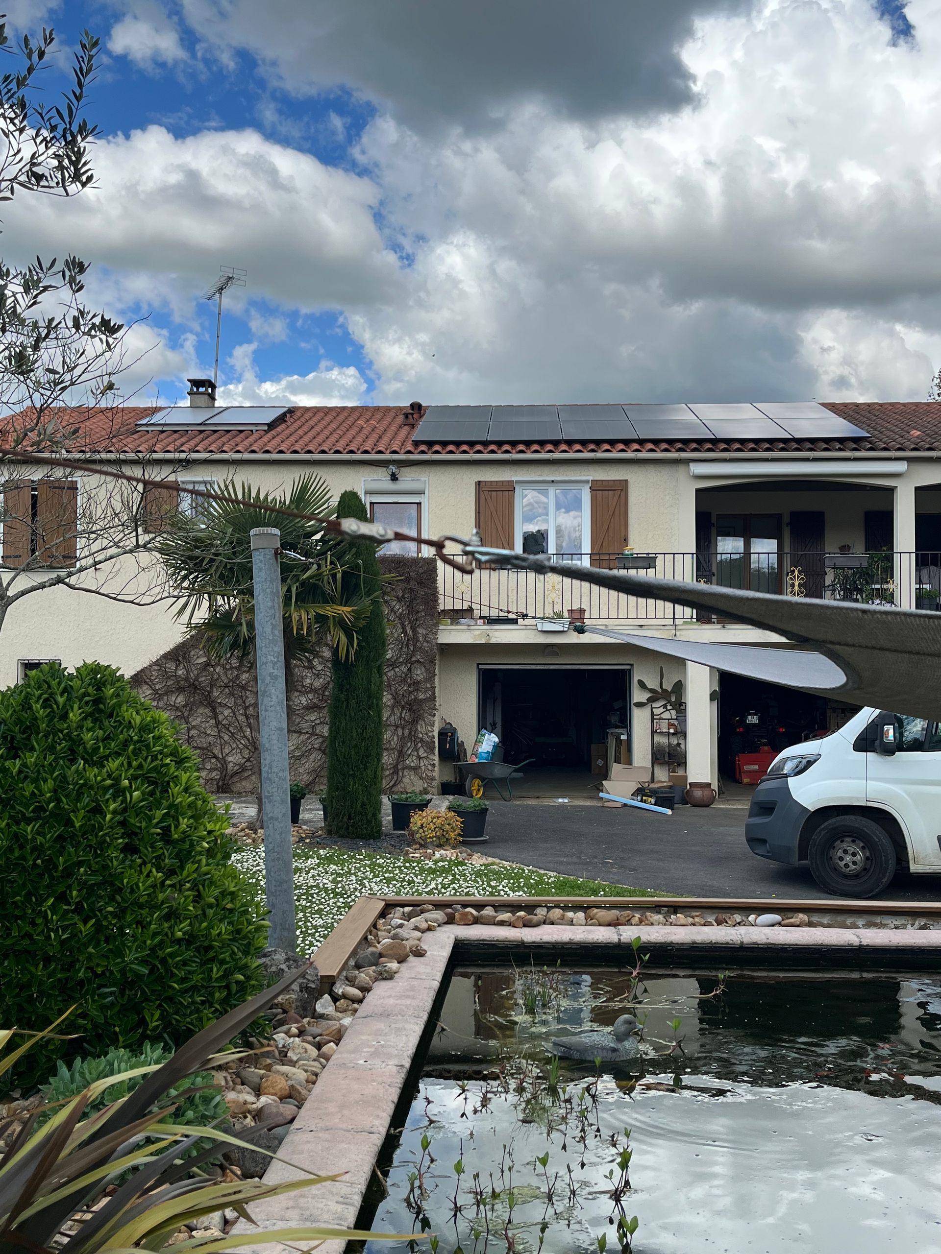 Cour intérieure avec bassin réfléchissant, allée en pierre, SUV blanc et maison à deux étages sous un ciel nuageux