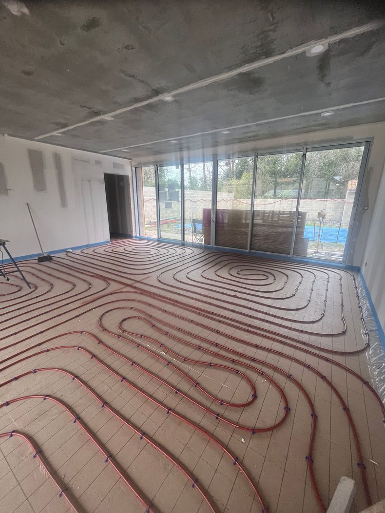 Pièce intérieure en construction avec des tubes de chauffage au sol rouges posés sur un sous-plancher blanc.