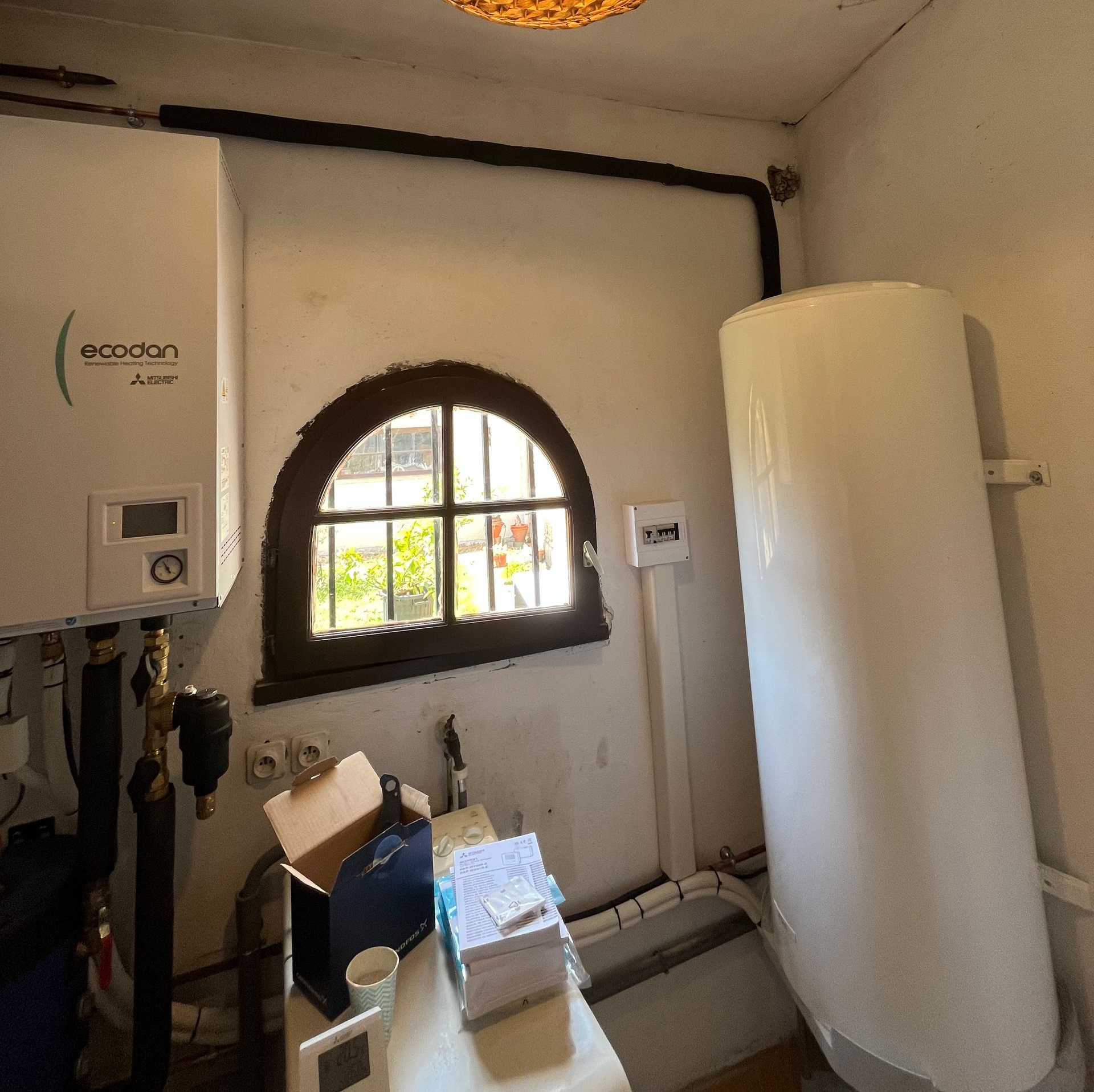 Petite buanderie avec fenêtre cintrée, commandes murales et grand réservoir d'eau blanc.