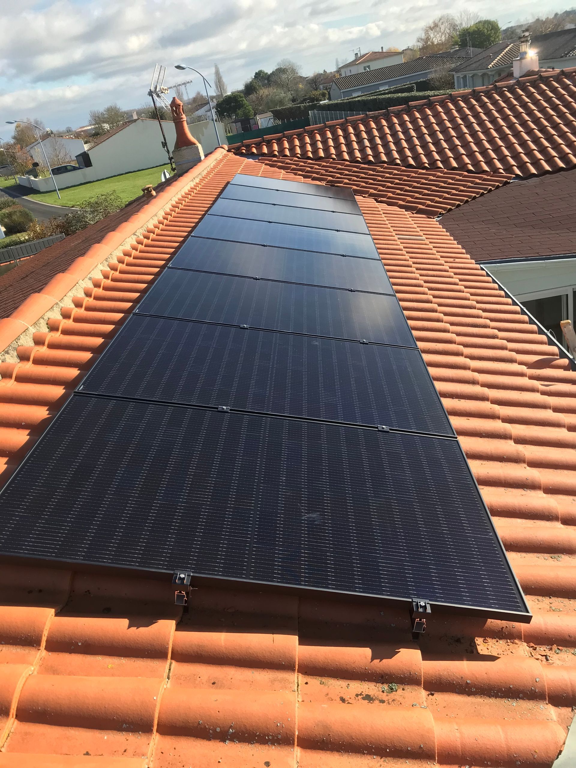 Panneaux solaires installés sur un toit de tuiles rouges sous un ciel partiellement nuageux