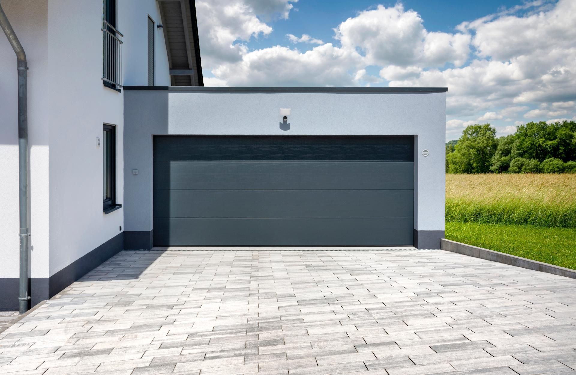 Modernes Haus mit grauem Doppelgaragentor und gepflasterter Auffahrt neben einem grasbewachsenen Feld.