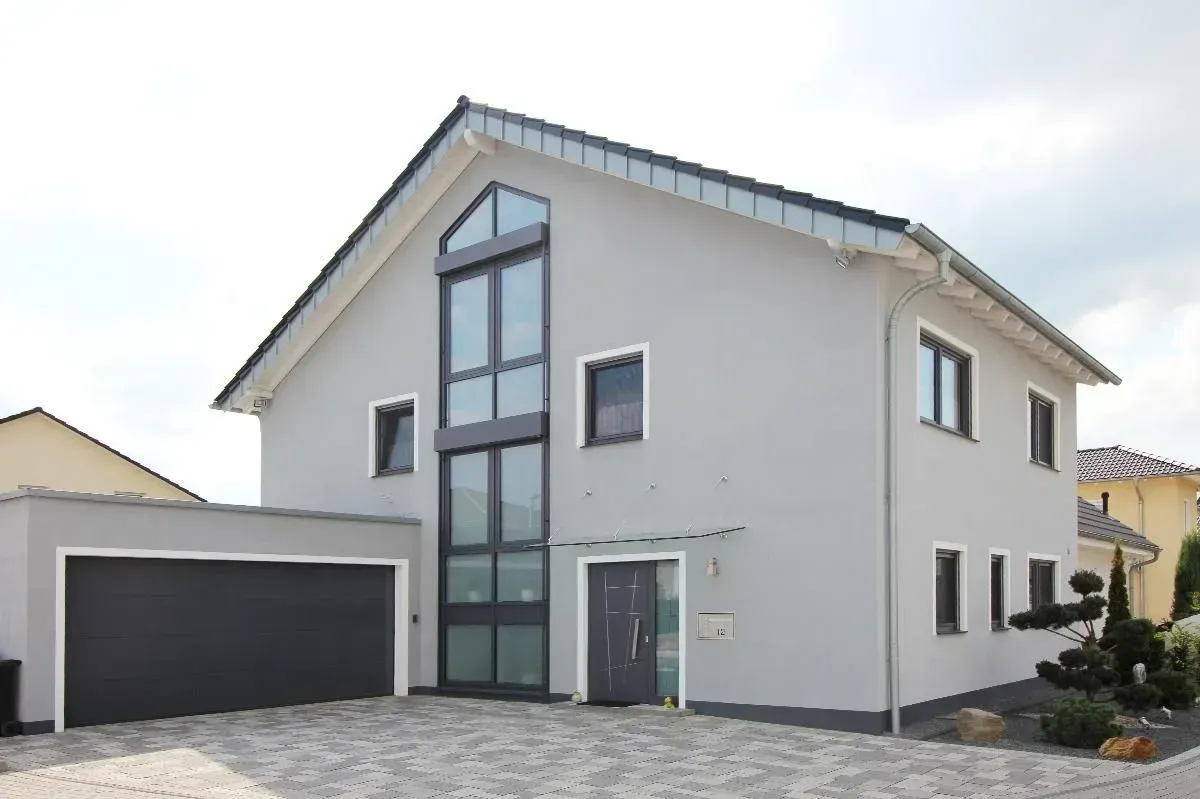 Modernes zweistöckiges Haus mit schwarzem Garagentor und hohem Glaseingang, gesehen von der Einfahrt aus.