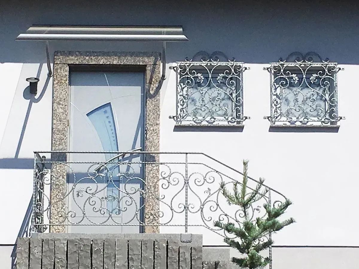 Weiße Hausfassade mit kunstvollem Balkongeländer, dekorativen Fenstergittern und einer Topfpflanze