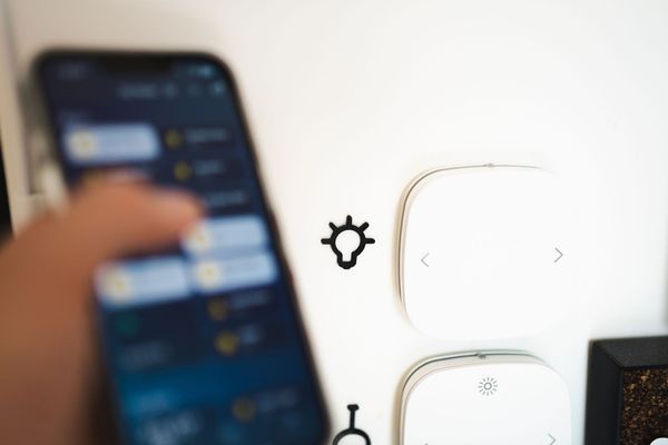 Main tenant un smartphone à côté d'interrupteurs de commande d'éclairage muraux