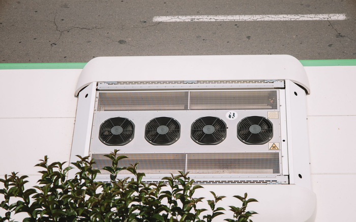 Quatre ventilateurs noirs dans une unité de ventilation blanche sur le toit, à côté de la verdure.