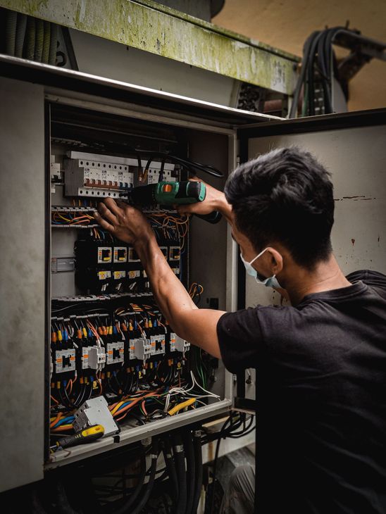 Un technicien inspecte un panneau de commande électrique ouvert, comportant des fils et des disjoncteurs.