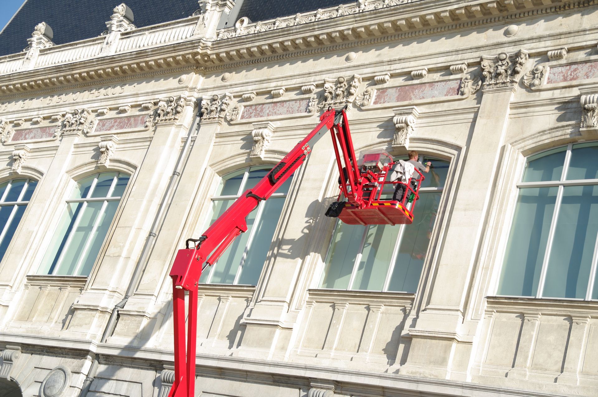 Nacelle élévatrice rouge avec un ouvrier qui répare la façade en pierre ouvragée d’un bâtiment historique