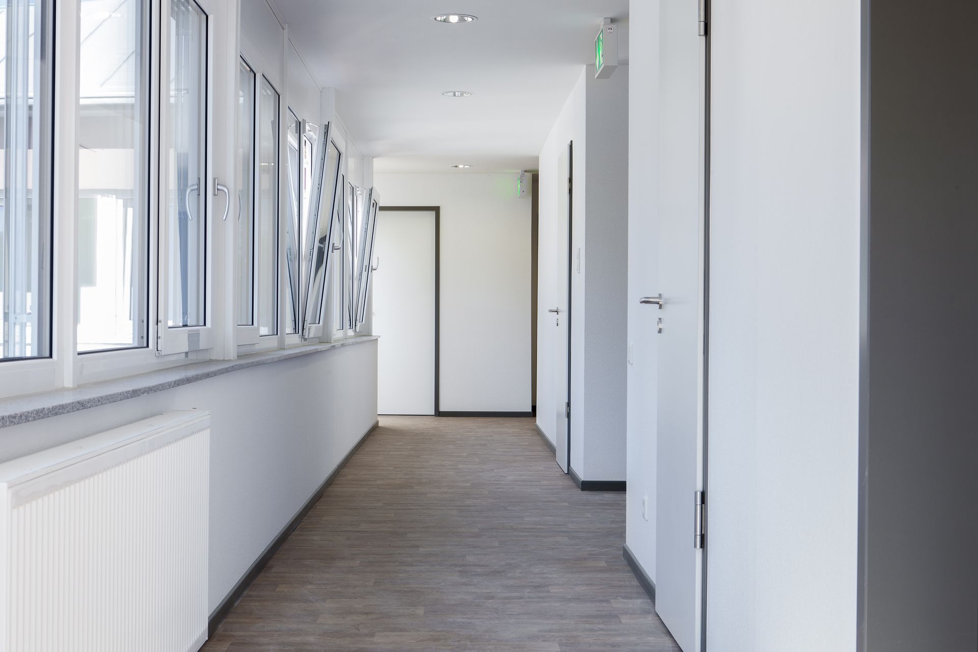 Couloir lumineux avec des murs blancs, des fenêtres, des portes et un parquet dans un bâtiment moderne