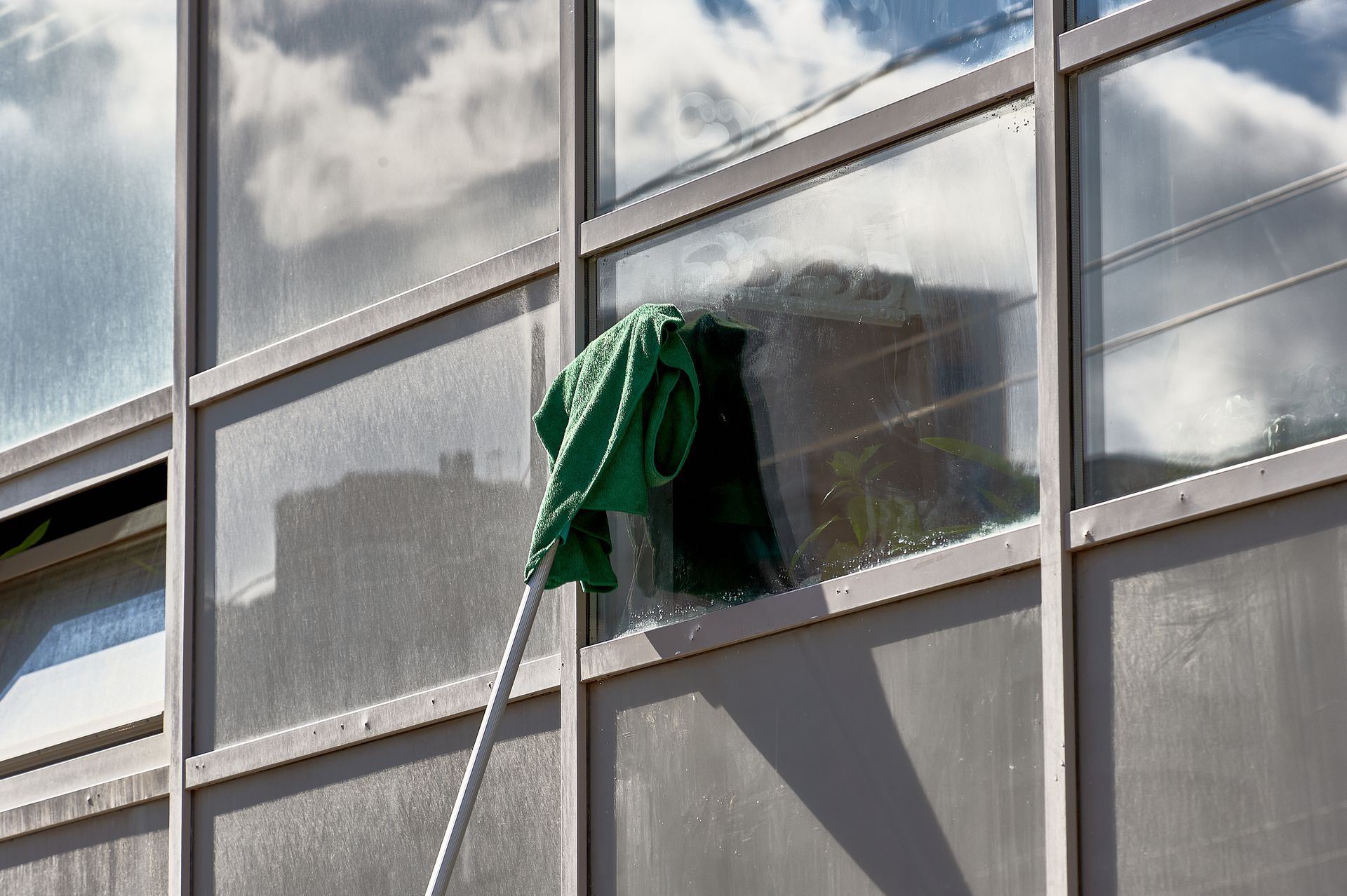 Un chiffon vert sur une perche nettoie la vitre d’un grand immeuble en verre