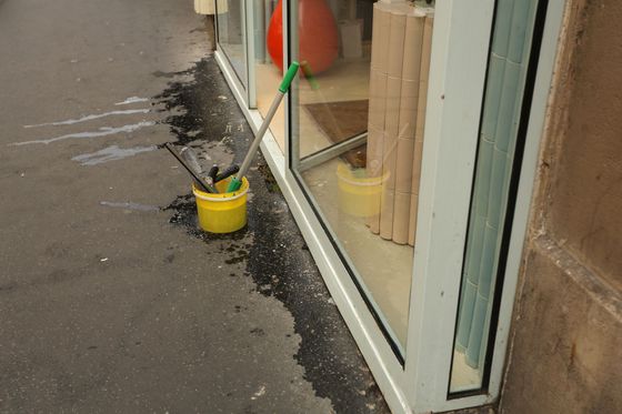 Trottoir mouillé devant la vitrine d’un magasin, avec un seau jaune et du matériel de nettoyage contre le mur