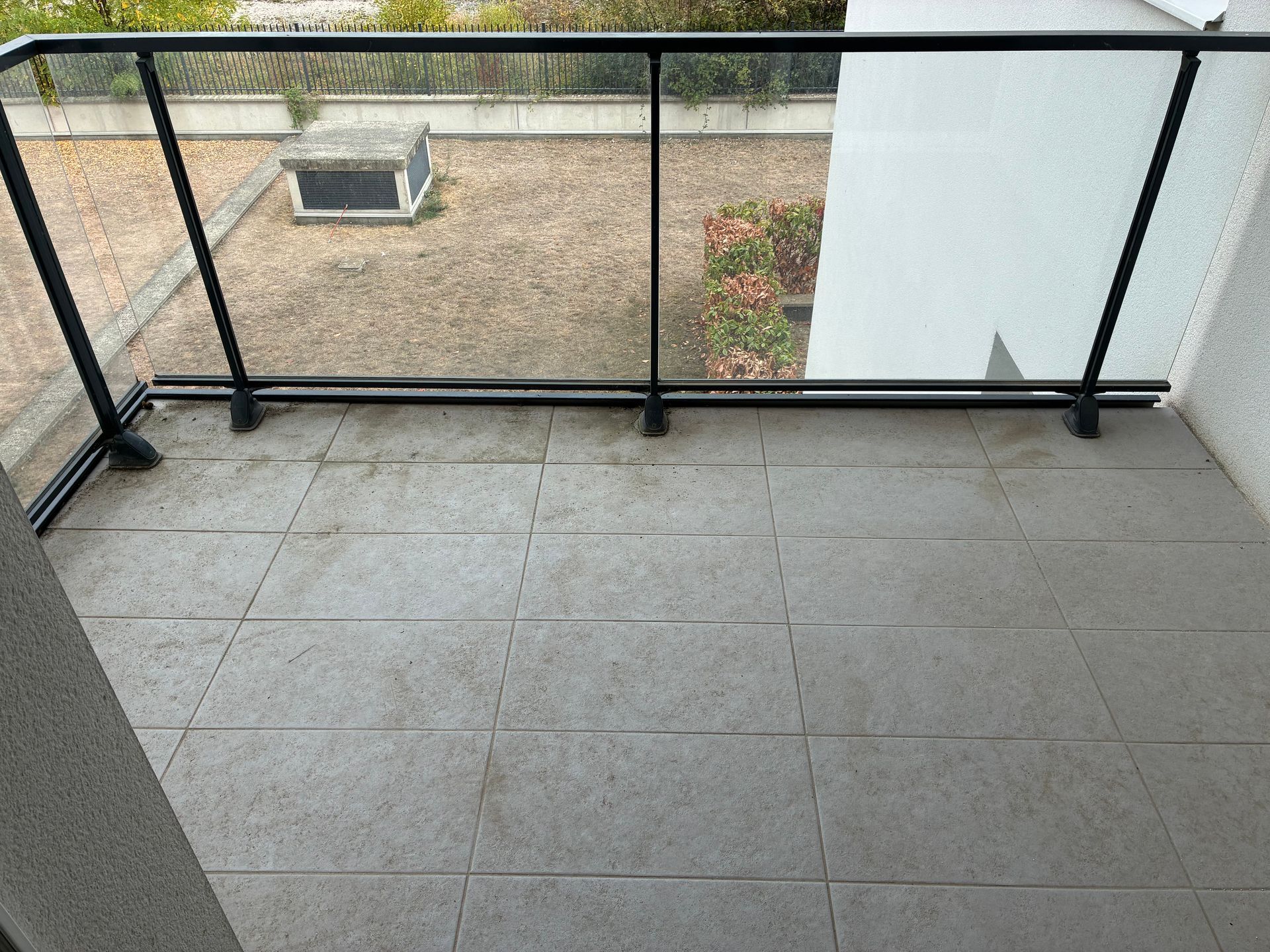 Balcon carrelé vide avec une rambarde noire donnant sur une cour.
