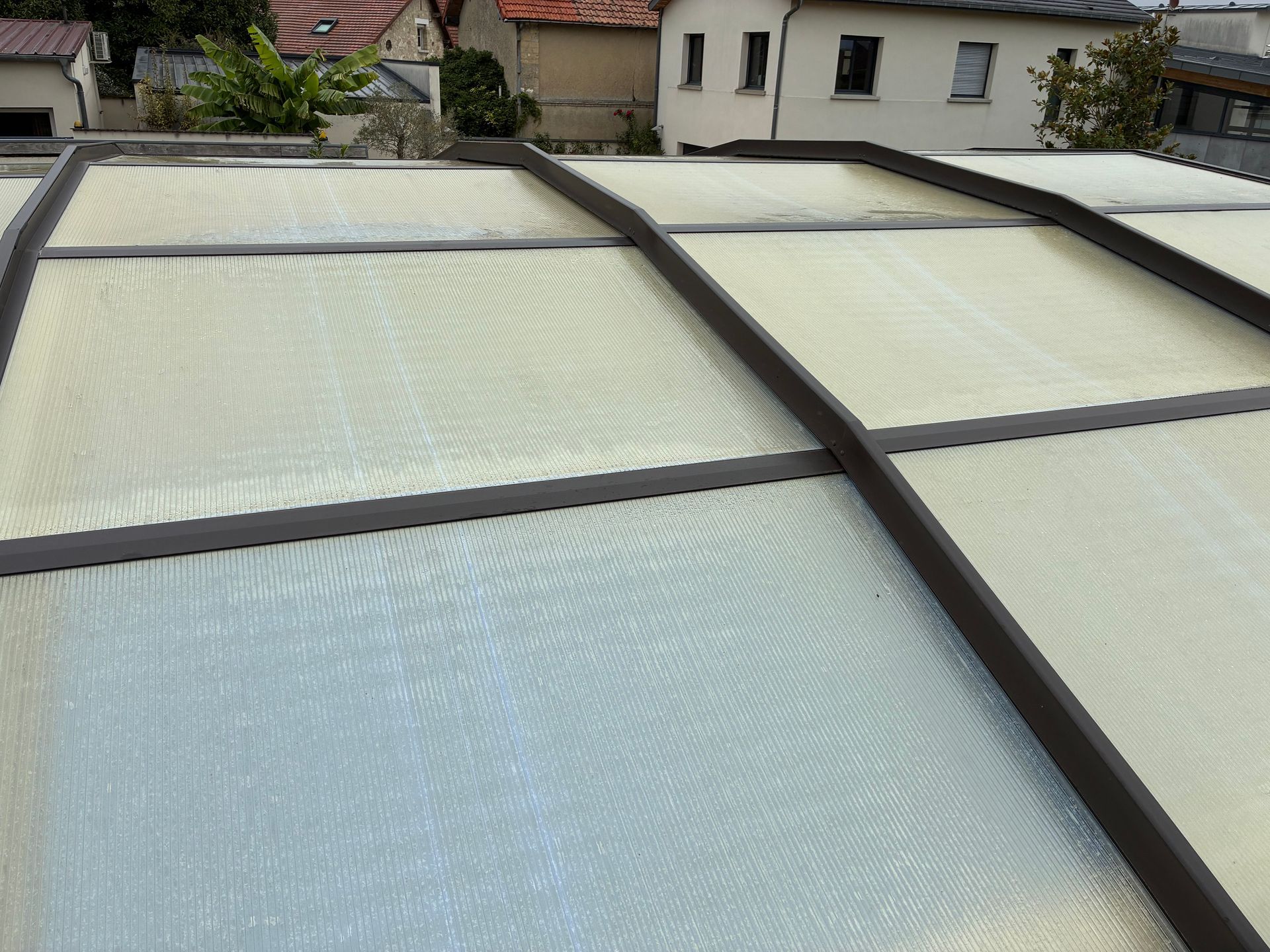 Panneaux translucides pour toiture de terrasse, avec des poutres foncées, donnant sur des maisons et de la verdure