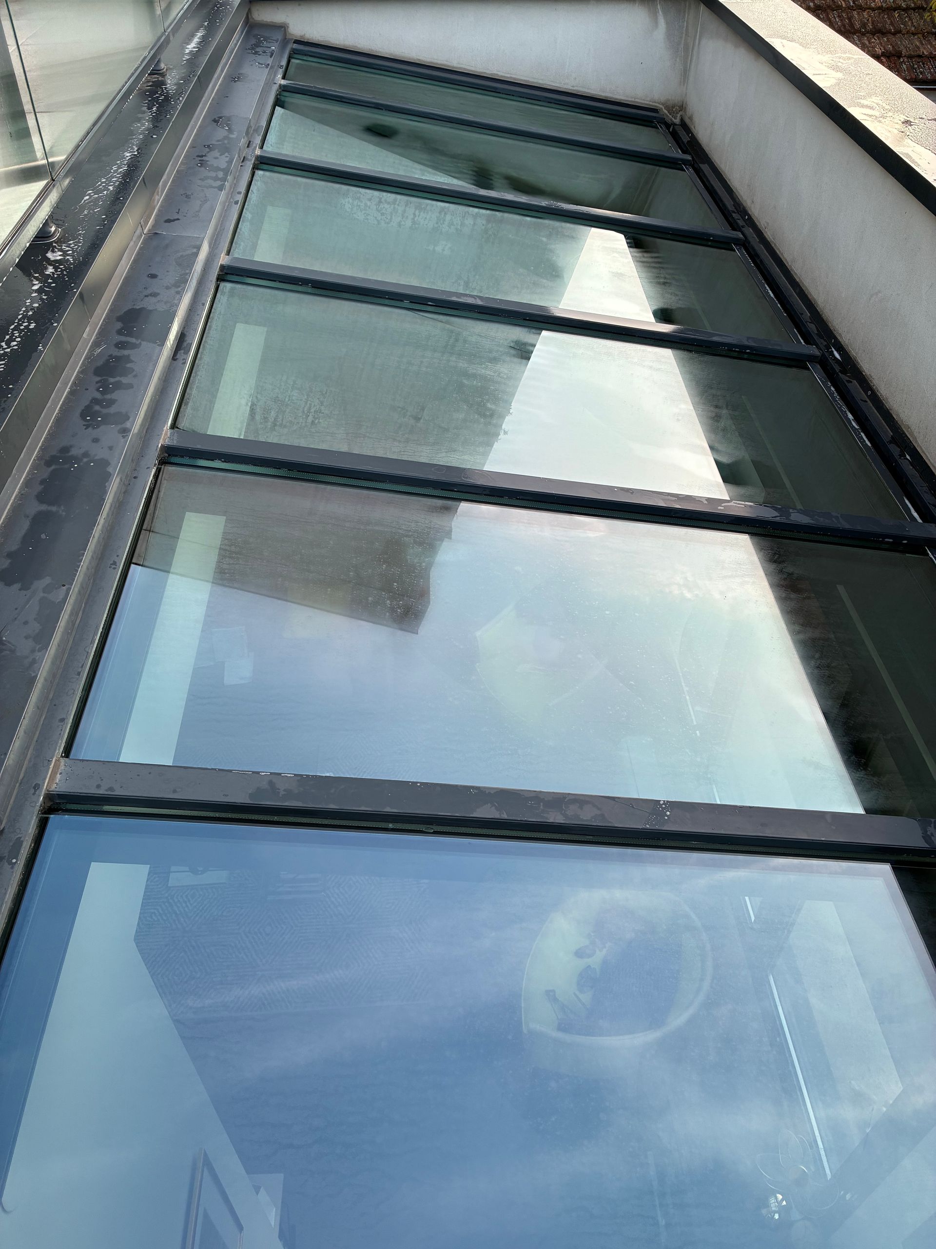 Vitrines en verre sous la façade d’un bâtiment, reflétant le ciel bleu et les nuages.