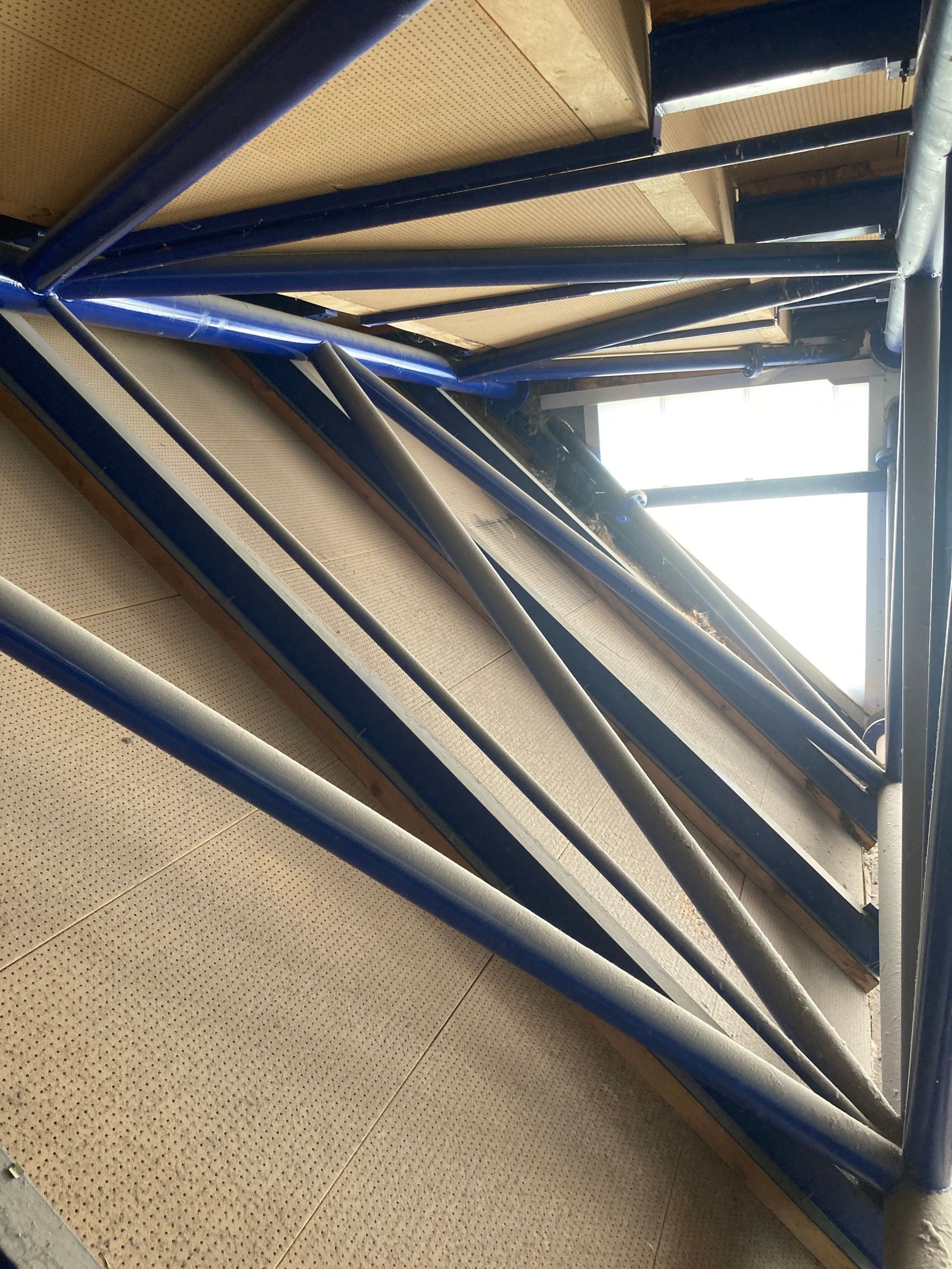 Structure d’escalier en métal bleu vue du dessous dans une cage d’escalier intérieure, avec une lumière vive en haut