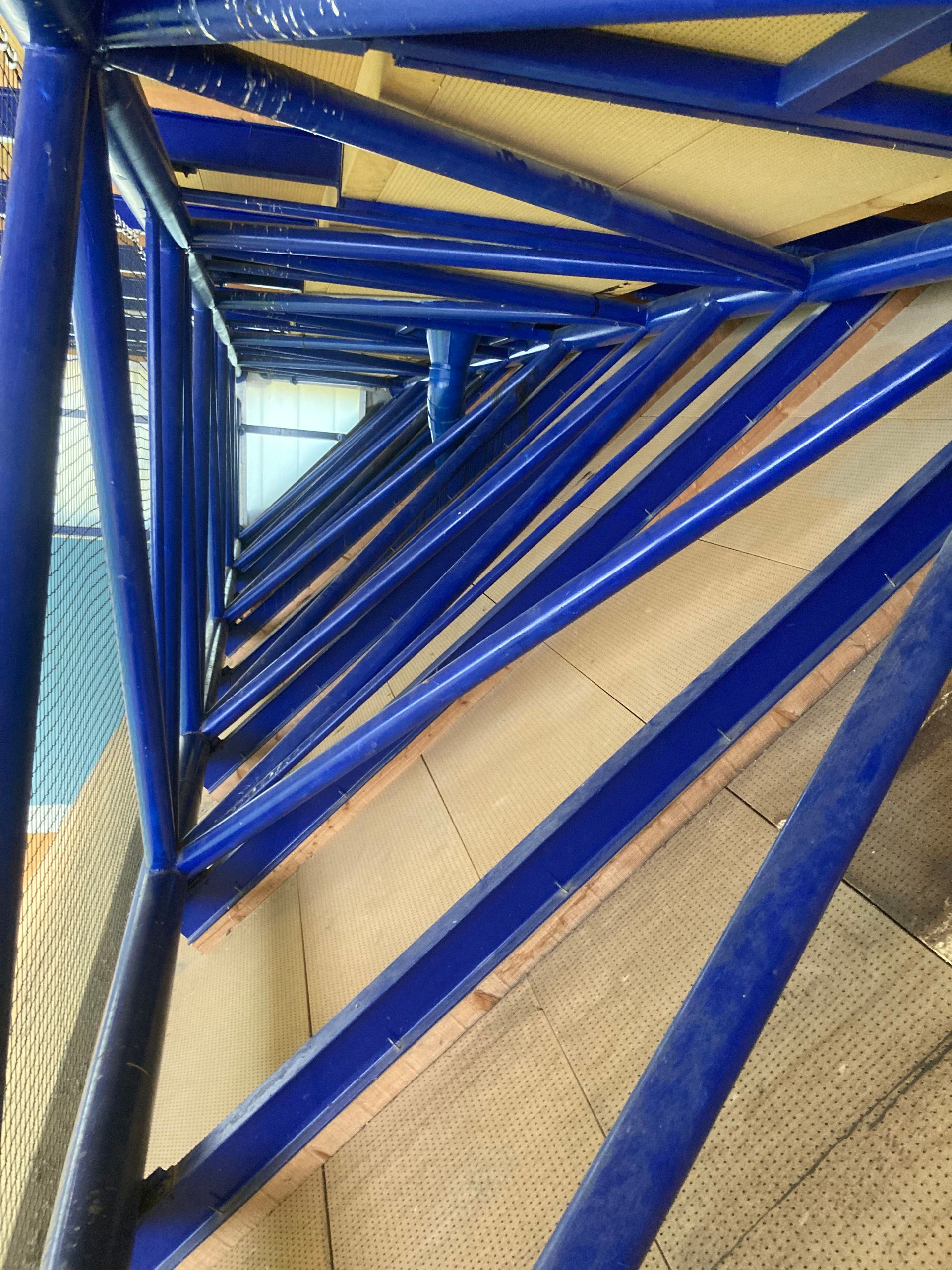Des poutres métalliques bleues formant une spirale triangulaire dans une structure architecturale intérieure