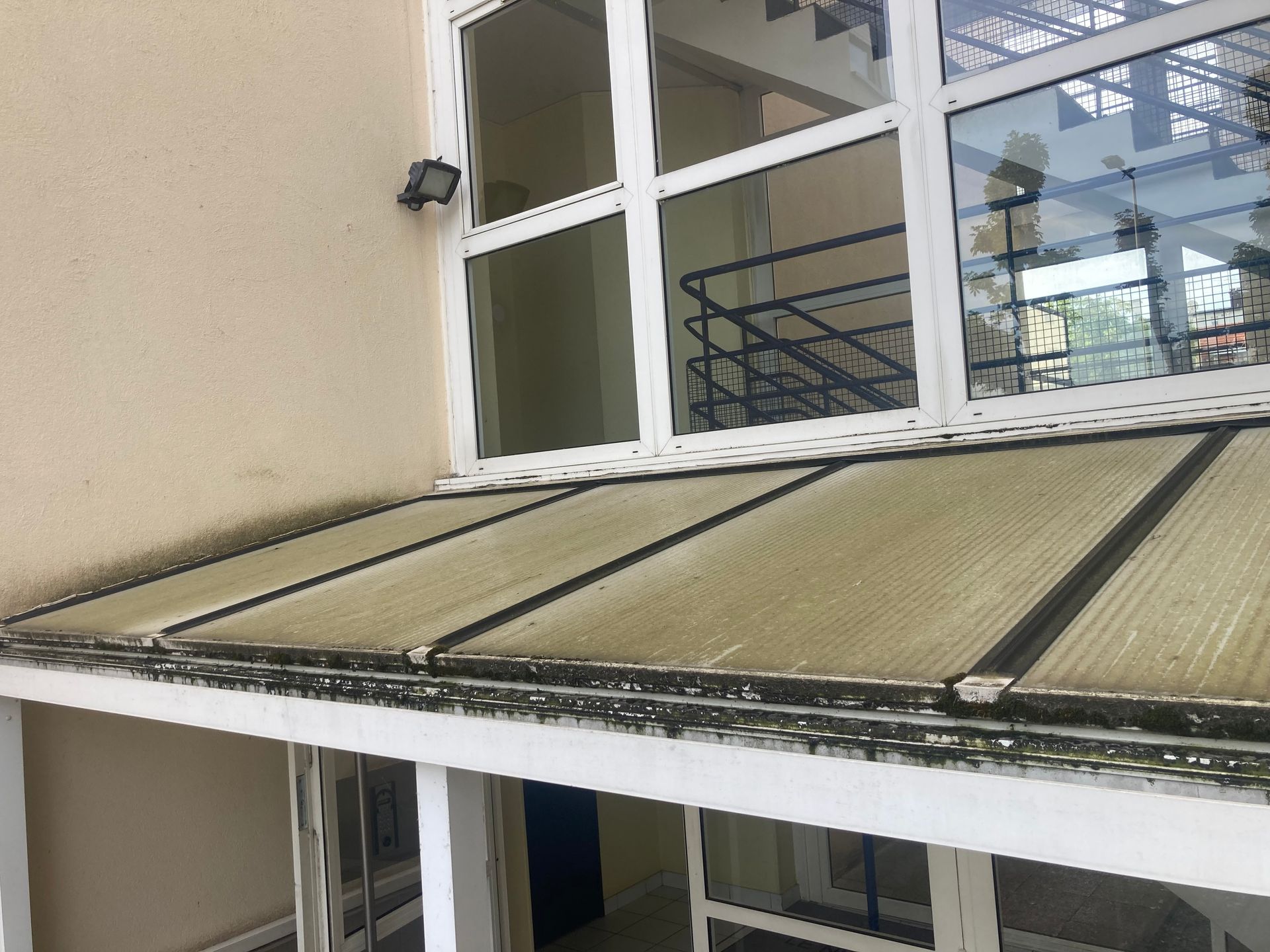 Auvent extérieur au-dessus d’une porte, avec des fenêtres à cadre blanc et un revêtement beige crème