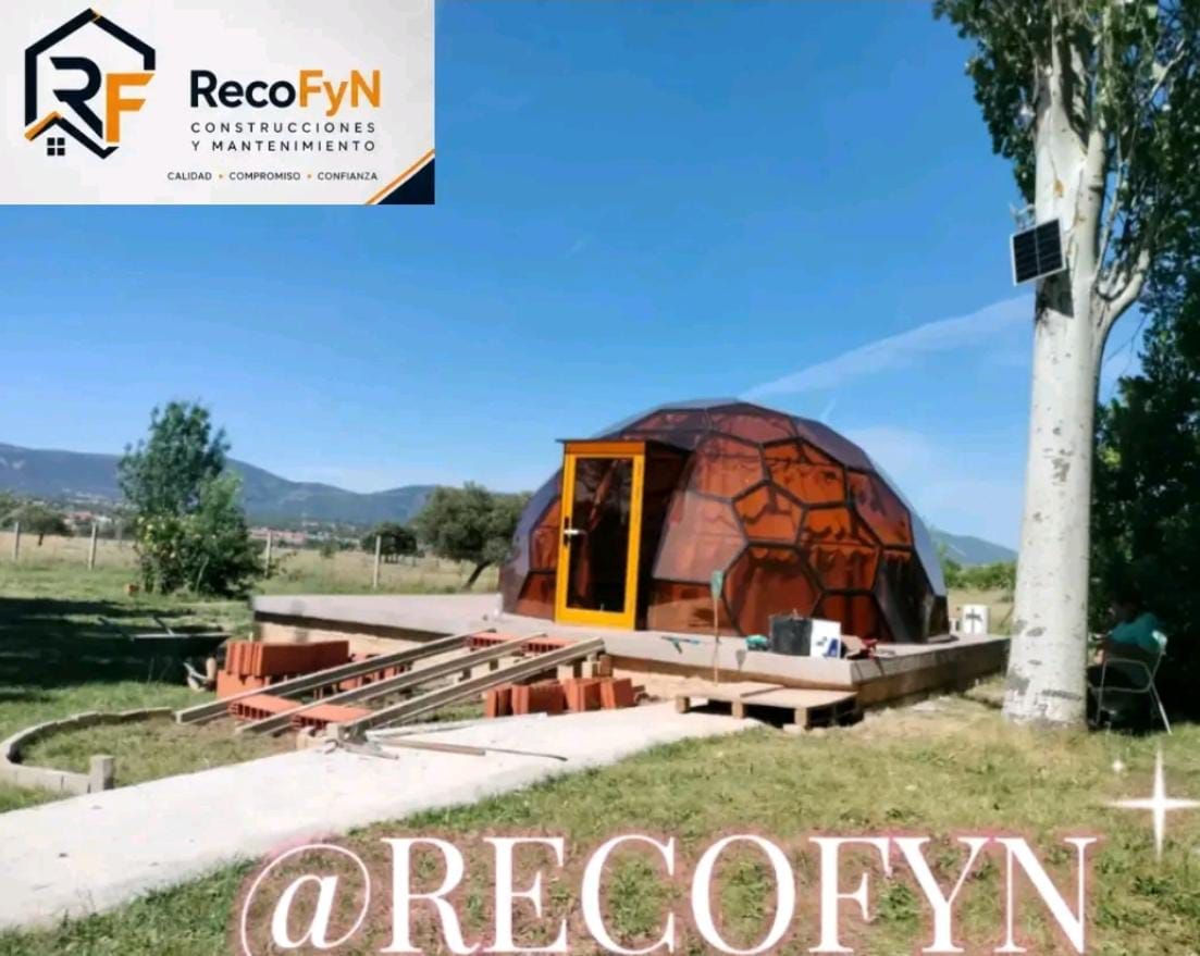 Cabaña con cúpula geodésica y terraza de madera en un paisaje rural cubierto de hierba bajo un cielo azul, con el logotipo y la marca de agua de Recofyn.
