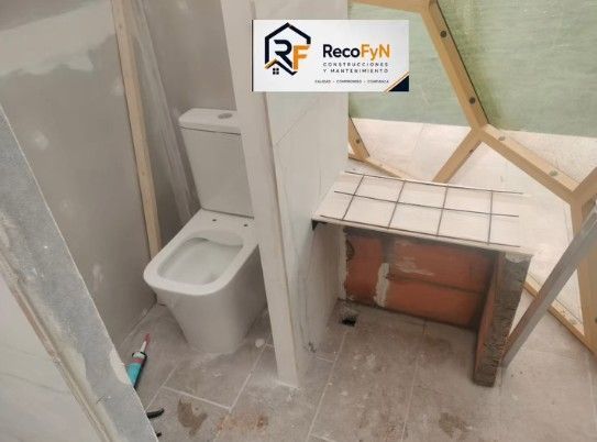 Baño pequeño con inodoro, lavabo alicatado y espejo o ventana rota encima del lavabo.
