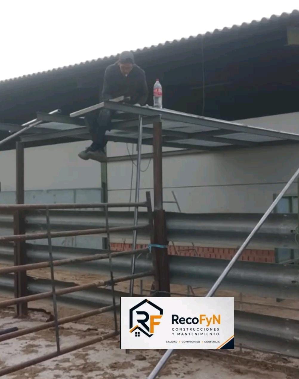 Persona sentada en un andamio metálico en una obra de construcción, sosteniendo una botella, con un techo encima.