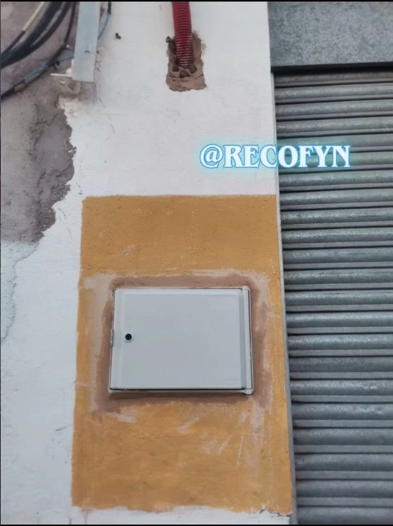 Caja eléctrica blanca en una pared color canela junto a una puerta metálica con contraventana.