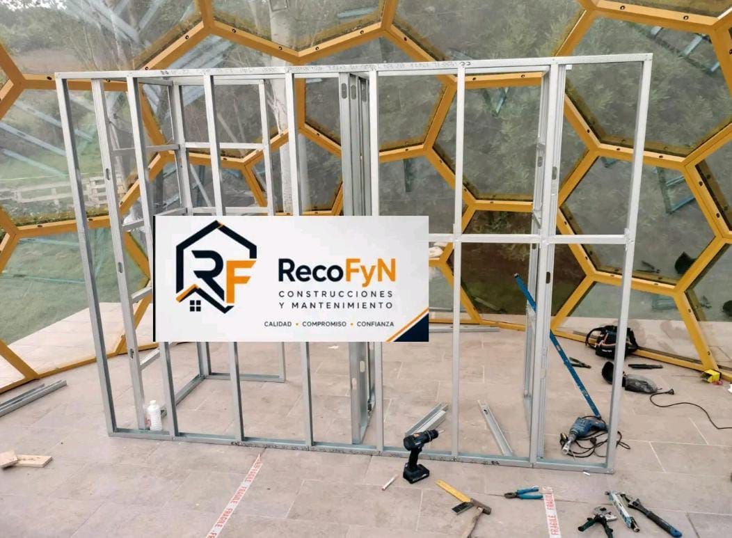 Estructura de acero en construcción con un letrero de RecoFYN al frente y una pared hexagonal decorativa detrás.