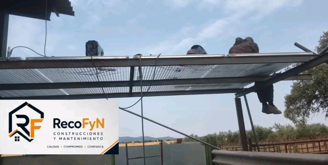 Trabajadores en la estructura metálica de un puente sobre una carretera, con el logotipo de RecoFYN en la parte inferior izquierda.