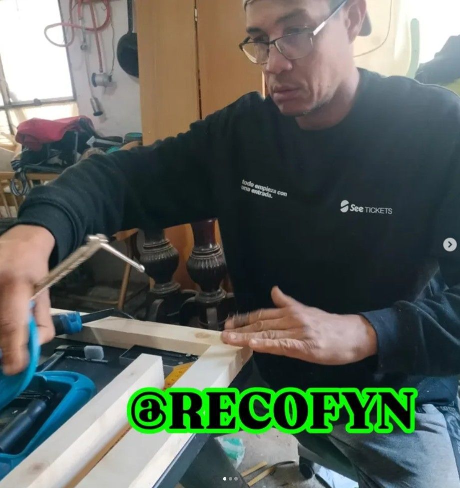 Persona trabajando con herramientas en un banco de trabajo en un taller, vistiendo una sudadera negra.
