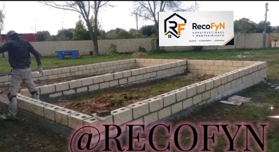 Obrero construyendo una base baja de ladrillo en una zona exterior cubierta de césped, con el letrero de RecoFYN al fondo.
