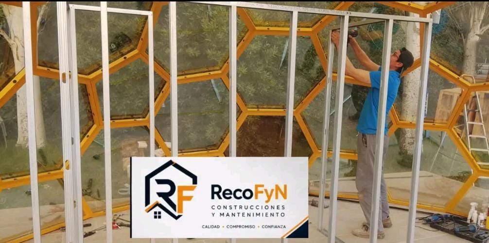 Un trabajador instala un panel de pared hexagonal de metal blanco con ribete naranja; se ve el logotipo de la marca RecoFYN.