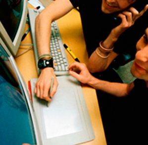 Dos personas sentadas en un escritorio mirando una pantalla de computadora