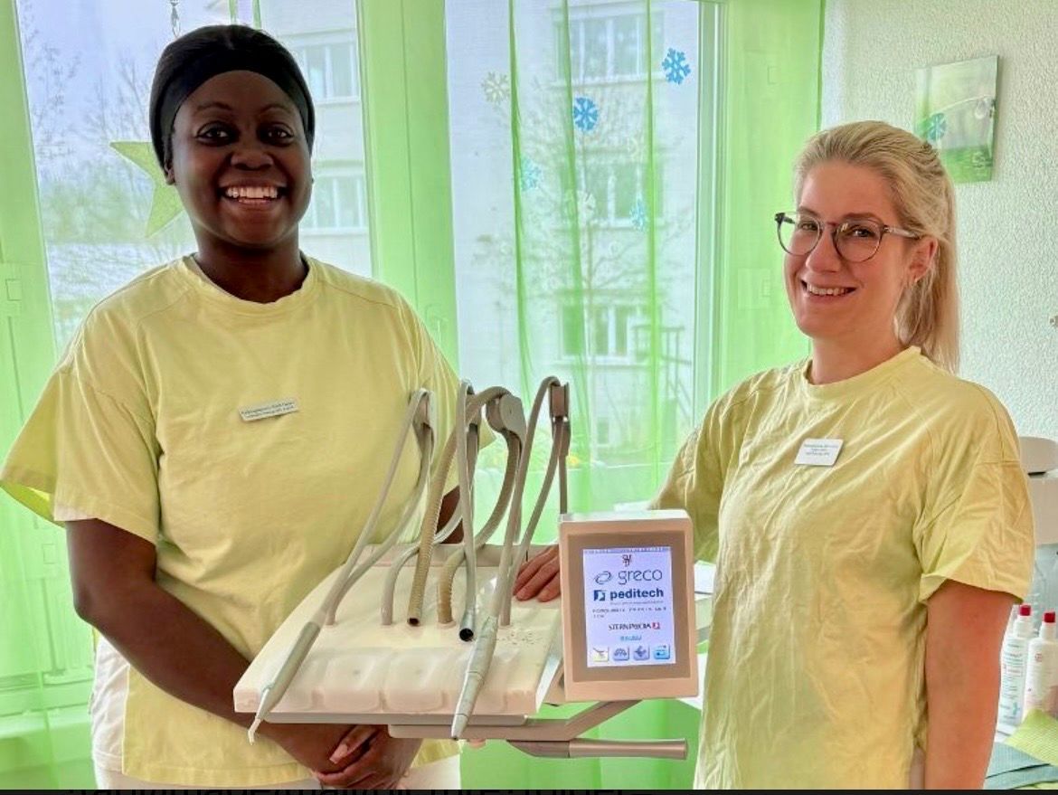 Zwei Zahnarzthelferinnen in hellgrünen Hemden lächeln und halten ein zahnärztliches Instrumentenset in einer Klinik.