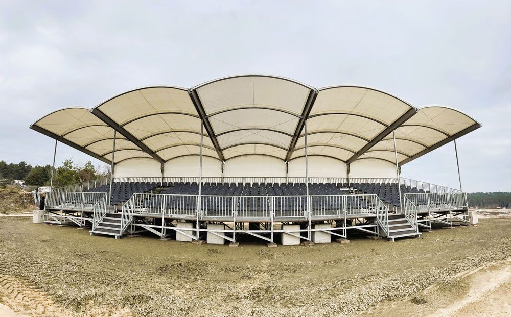 Circular outdoor stage with white canopy, gray railing, and steps, on muddy ground under overcast sky.