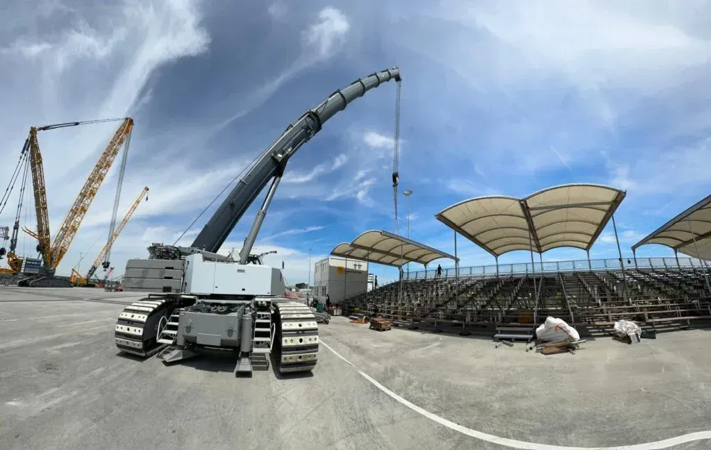 Kran auf Gleisen in der Nähe eines im Bau befindlichen Stadions, blauer Himmel, weiße Wolken.