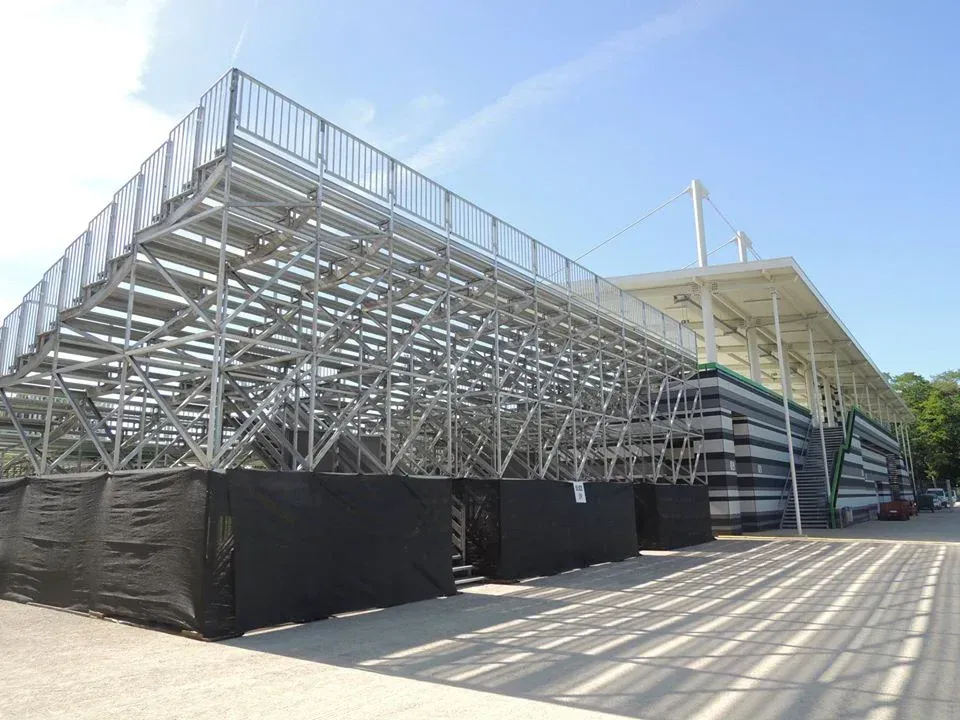 Metalltribünen mit schwarzen Umrandungen, eine sonnige Außenkulisse.