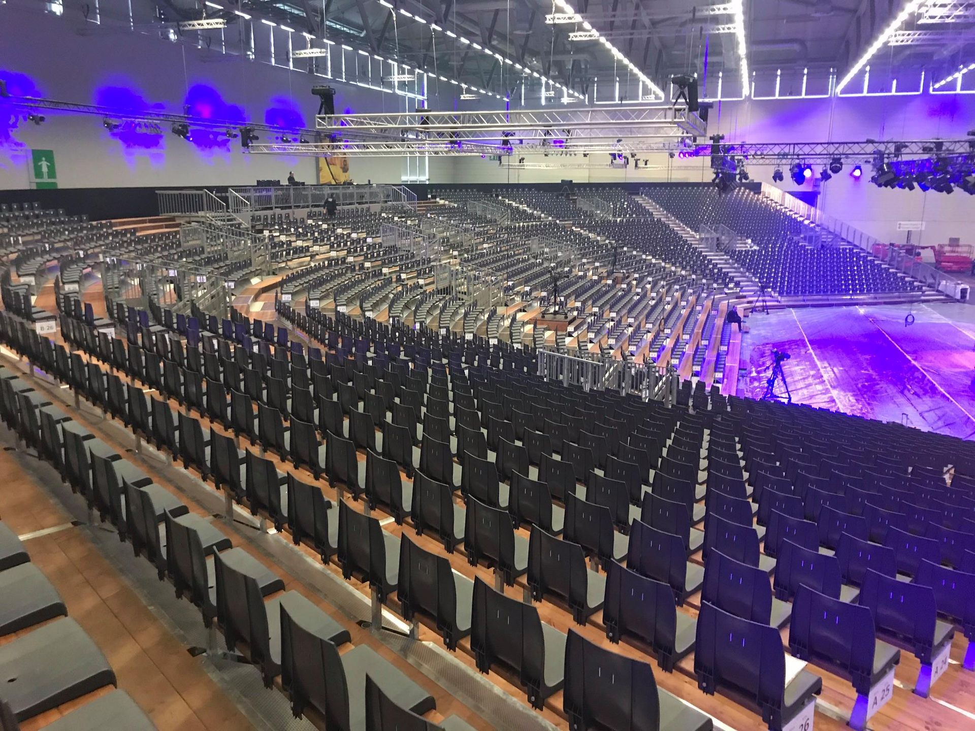 Reihen leerer, dunkler Sitze füllen eine große, mit Beleuchtungskörpern ausgestattete Indoor-Arena rechts auf der Bühne.