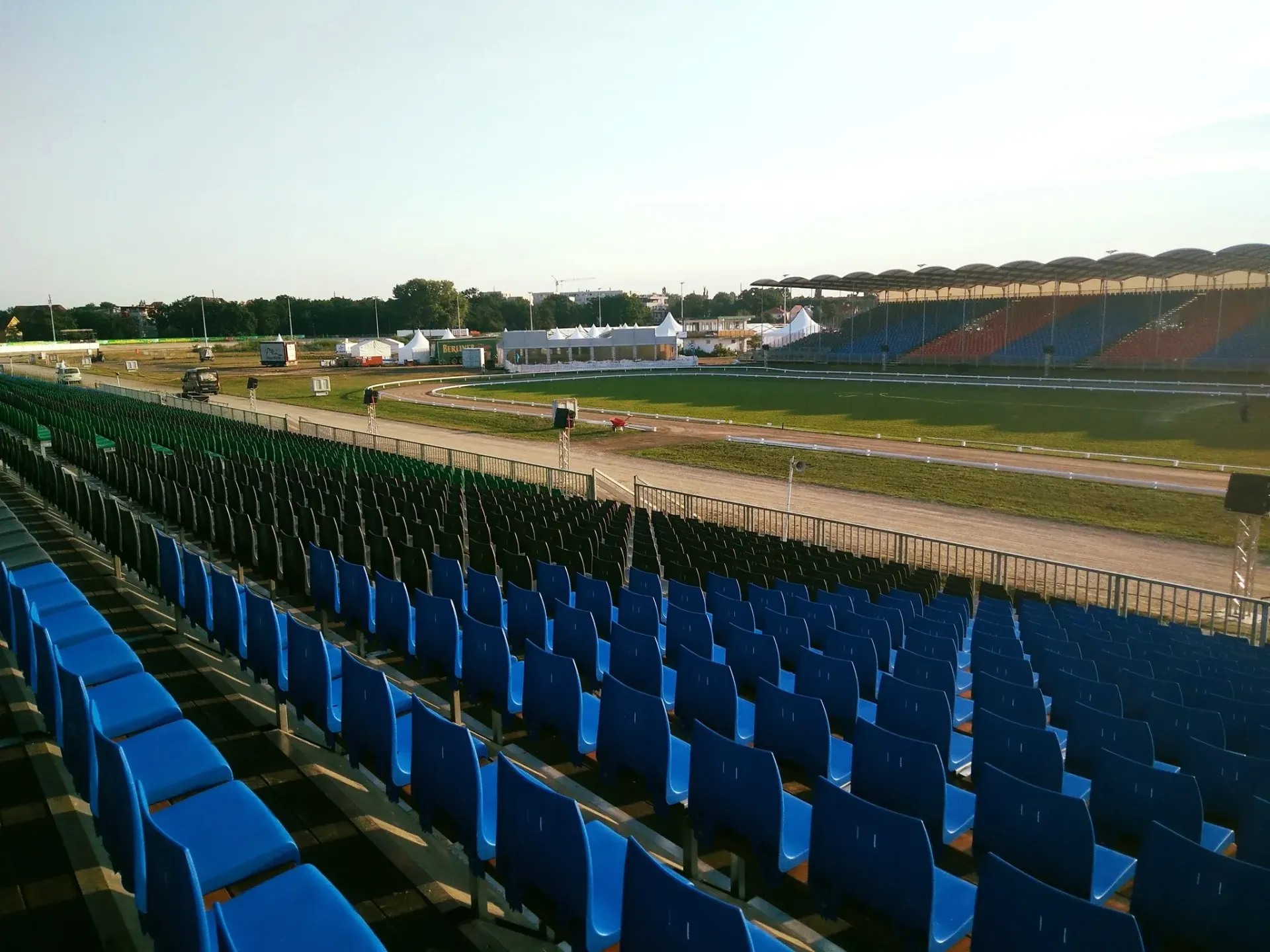 Reihen blauer und grüner Stadionsitze gegenüber einer Rennstrecke und in der Ferne ein weißes Zelt unter einem klaren Himmel.