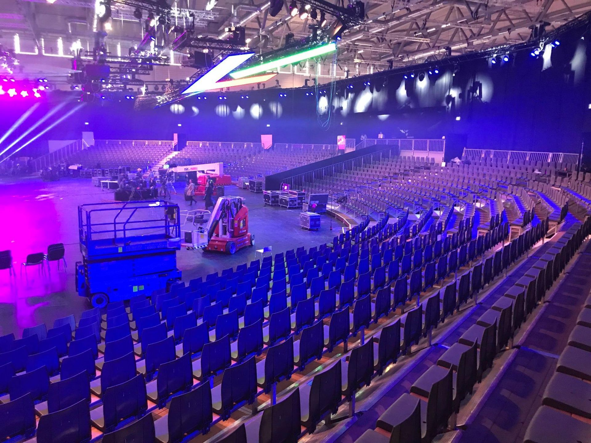 Große leere Arena mit Reihen blauer Sitze, Bühnenaufbau und Beleuchtung.