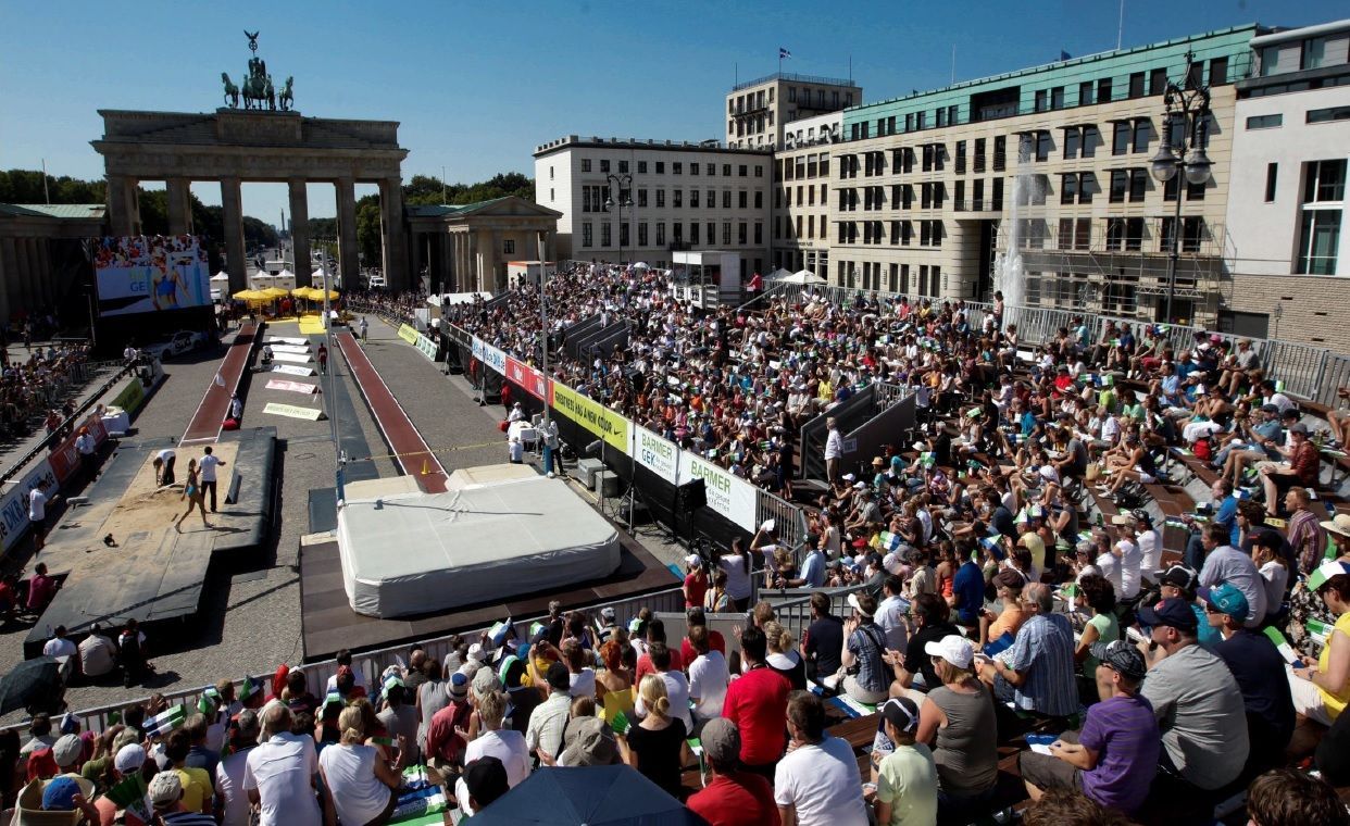 Stabhochsprung-Wettbewerb am Brandenburger Tor, Berlin. Große Menschenmenge schaut den Athleten zu.